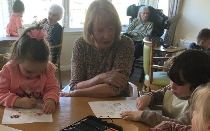 older lady sat with some children colouring